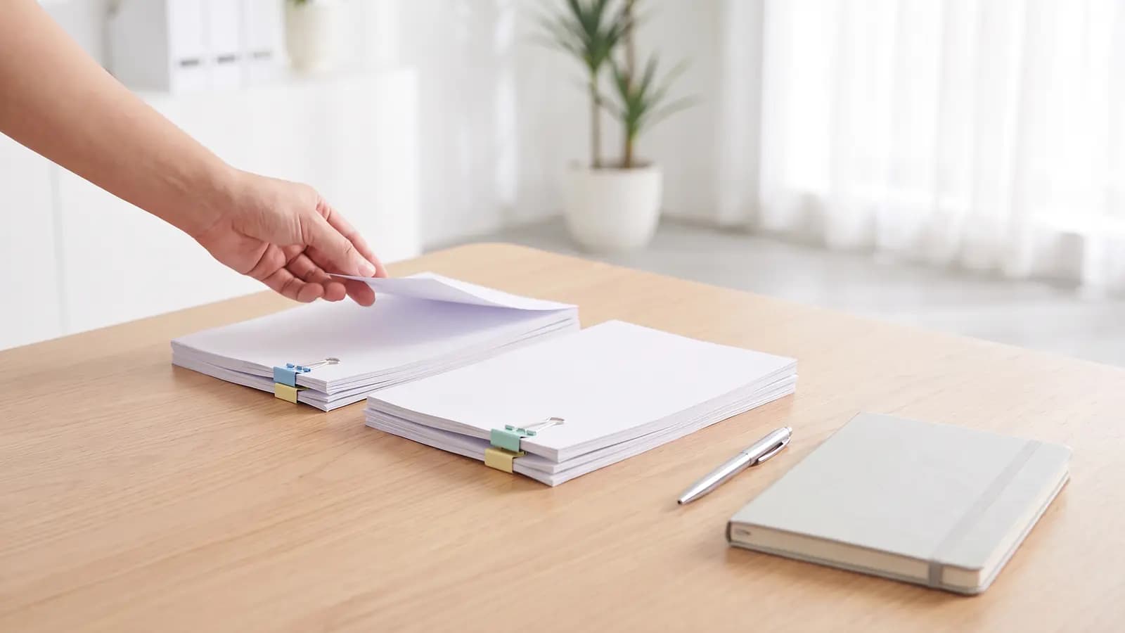 Facturas impresas ordenadas en dos pilas sobre un escritorio claro, cada una con clips de colores, junto a una libreta.